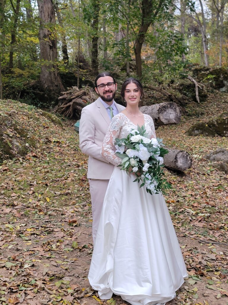 Matthew and Abigail standing together at the altar of God's Cathedral at The Cove, the outdoor woodland ceremony site at Timber Valley Farm Barn Rental, surrounded by tall trees.