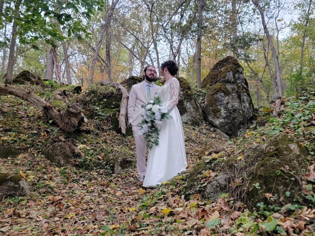 Matthew and Abigail walking together through the narrow natural stone and tree-lined passage exiting The Cove at Timber Valley Farm Barn Rental Wedding and Event Venue.