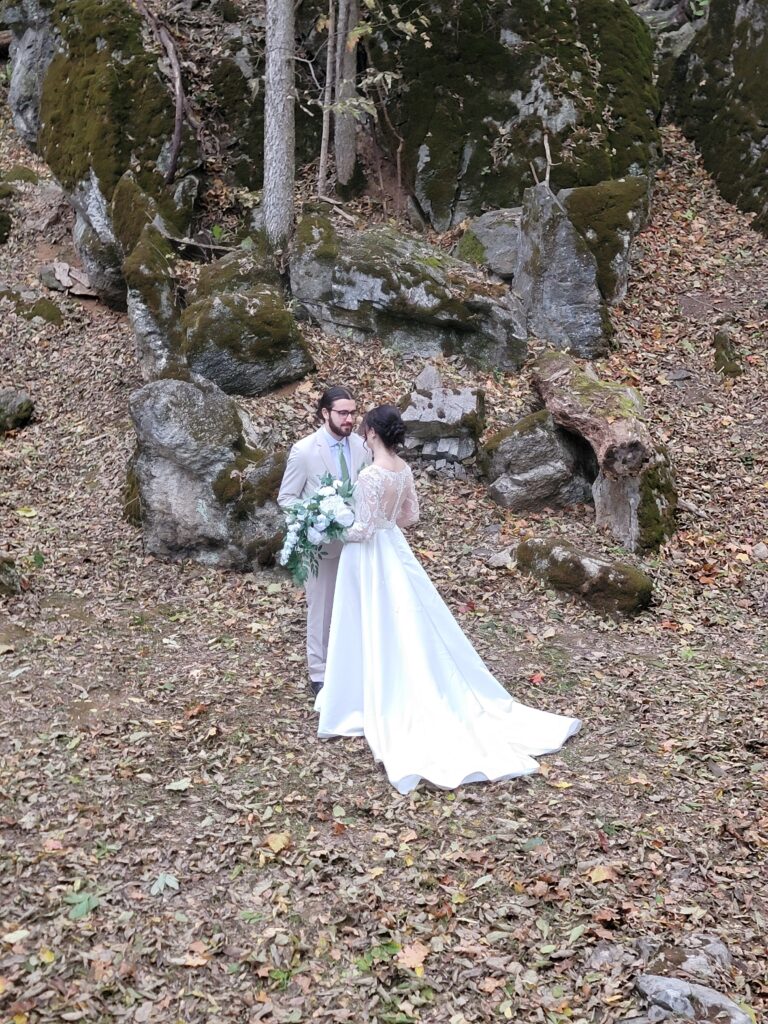 Matthew and Abigail facing each other in the Maryland woods in The Cove at Timber Valley Farm Barn Rental Wedding and Event Venue, with her white wedding dress flowing elegantly over a bed of fallen autumn leaves.