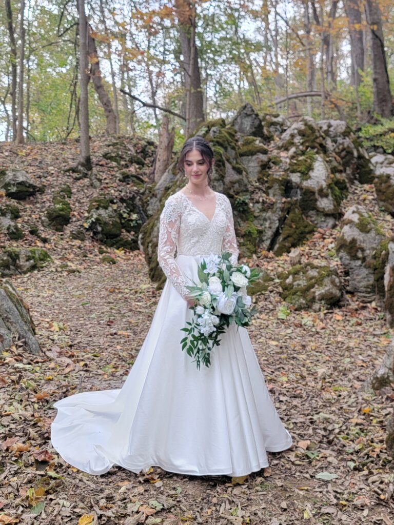 Abigail standing in the natural woodland setting of The Cove at Timber Valley Farm Barn Rental Wedding and Event Venue, with massive moss-covered boulders.