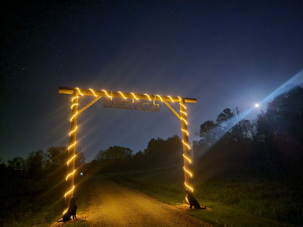 Illuminated Timber Valley driveway entrance arch under a moonlit sky at Timber Valley Farm Barn Rental in Clear Spring, Maryland.