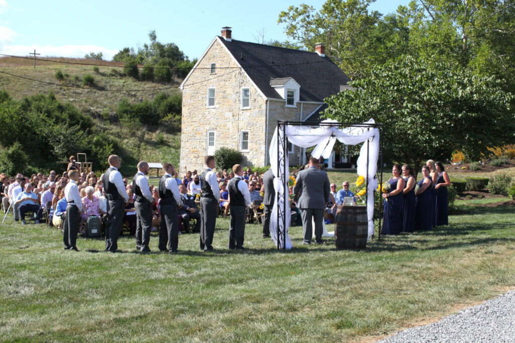 Outdoor wedding ceremony at the Wedding Arch with the historic stone farmhouse in the background at Timber Valley Farm Barn Rental in Clear Spring, Maryland.