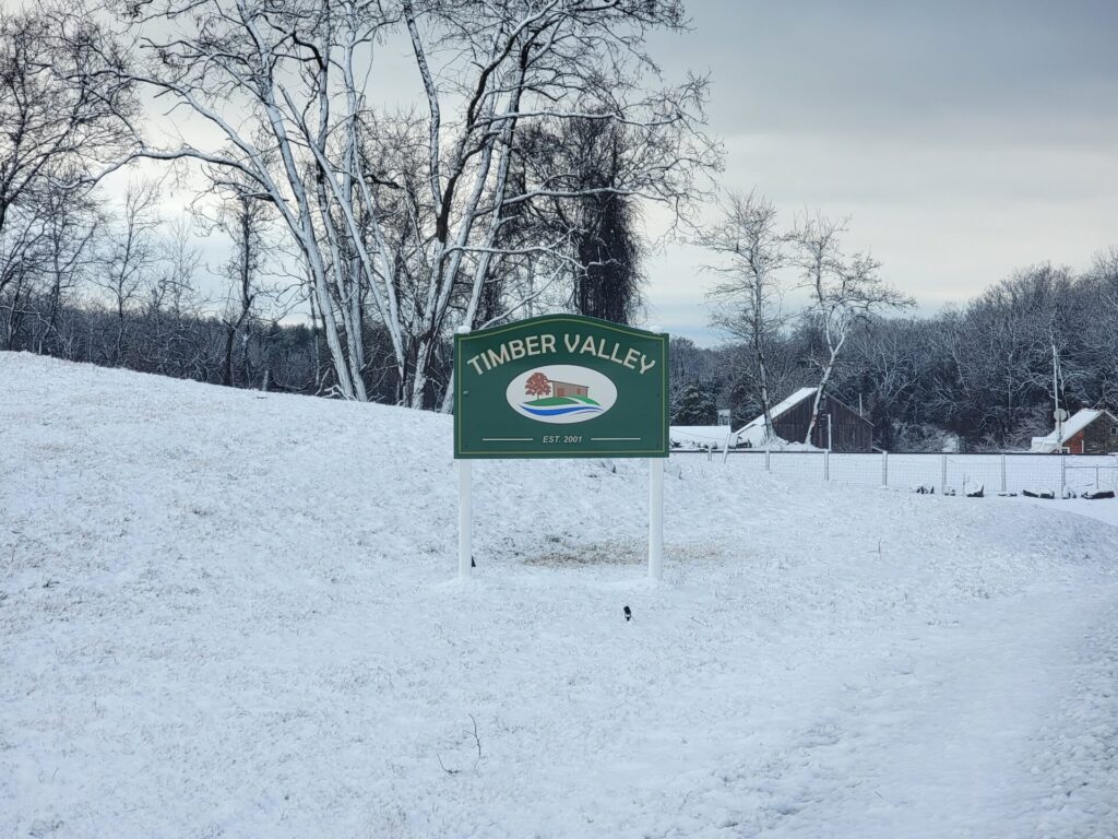 Snow-covered Timber Valley Farm entrance sign welcomes visitors to Timber Valley Farm Barn Rental, a peaceful Snow Wedding Venue Maryland surrounded by the winter countryside of Washington County.