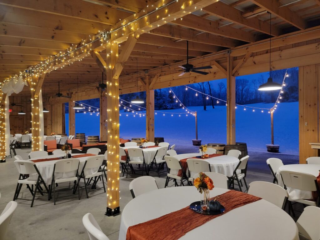 Snow at Timber Valley viewed from inside Timber Valley Farm Barn Rental, where warm lights, timber beams, and a snow-covered countryside create a welcoming winter gathering place.