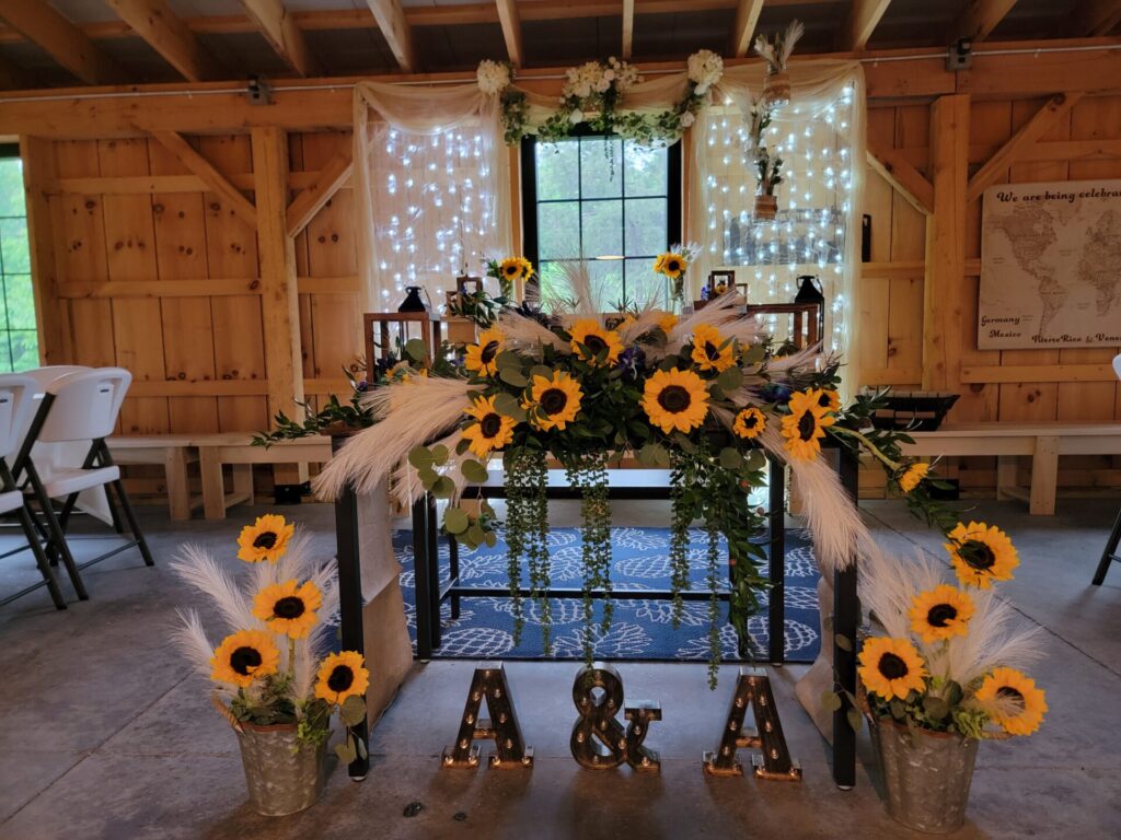 Rustic timber-frame barn interior featuring a beautifully decorated sweetheart table with sunflowers, twinkle lights, and handcrafted wood details at Timber Valley Farm Barn Rental in Clear Spring, Maryland.