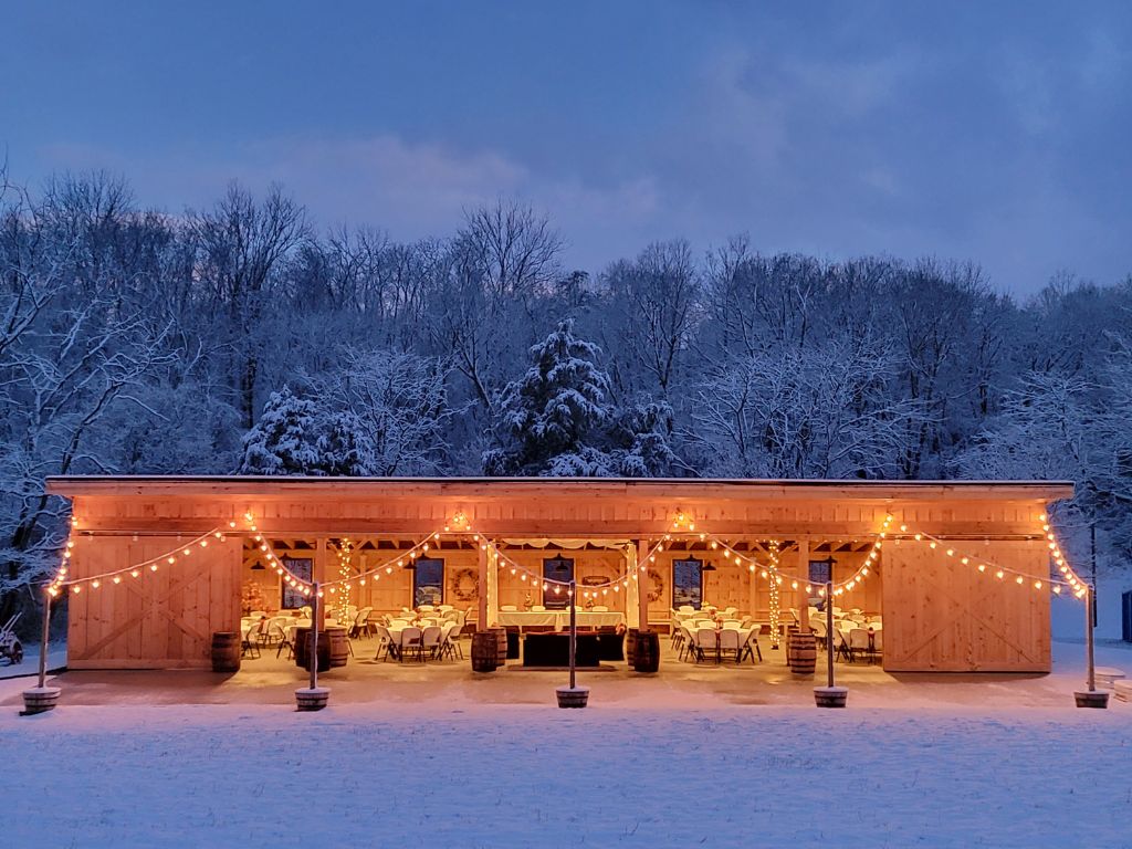 Snow Wedding Venue Maryland featuring the warmly illuminated timber frame barn at Timber Valley Farm Barn Rental surrounded by fresh snow and peaceful winter woodlands in Washington County, Maryland.