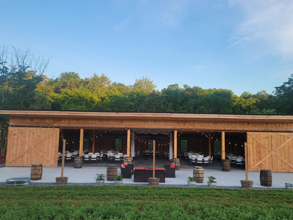 Outdoor wedding reception venue Maryland with open timber-frame barn, outdoor patio, seating, string lights, and wooded surroundings at Timber Valley Farm Barn Rental