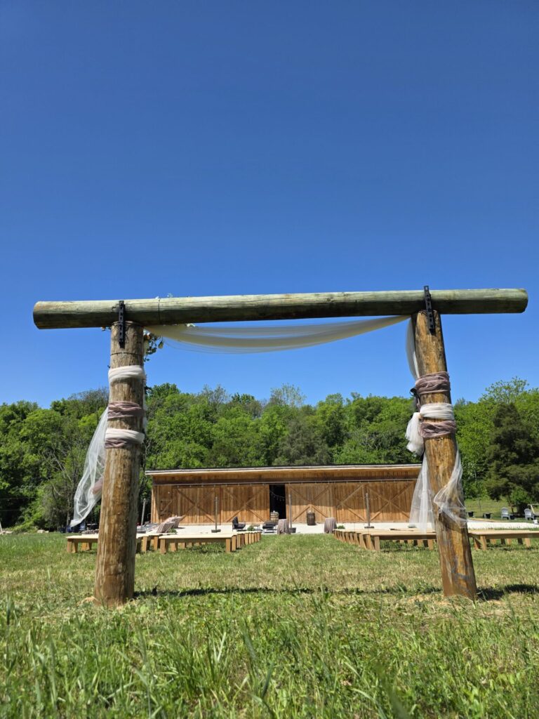 Outdoor Wedding Backdrop featuring the Wedding Ceremony Arbor, timber-frame barn, ceremony seating, and countryside at Timber Valley Farm Barn Rental in Clear Spring, Maryland.