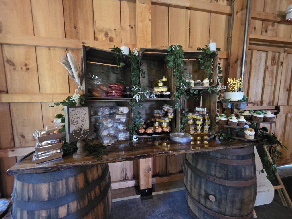 Wedding Reception Ideas featuring a rustic dessert station displayed on a handcrafted whiskey barrel table inside the timber frame barn at Timber Valley Farm Barn Rental in Clear Spring, Maryland.