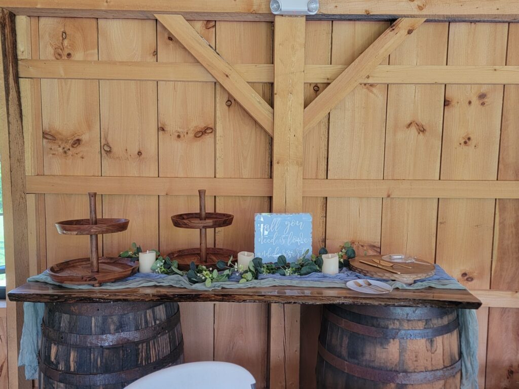 Wedding Reception Tables featuring a handcrafted live-edge display table supported by authentic whiskey barrels inside the timber frame barn at Timber Valley Farm Barn Rental in Clear Spring, Maryland.