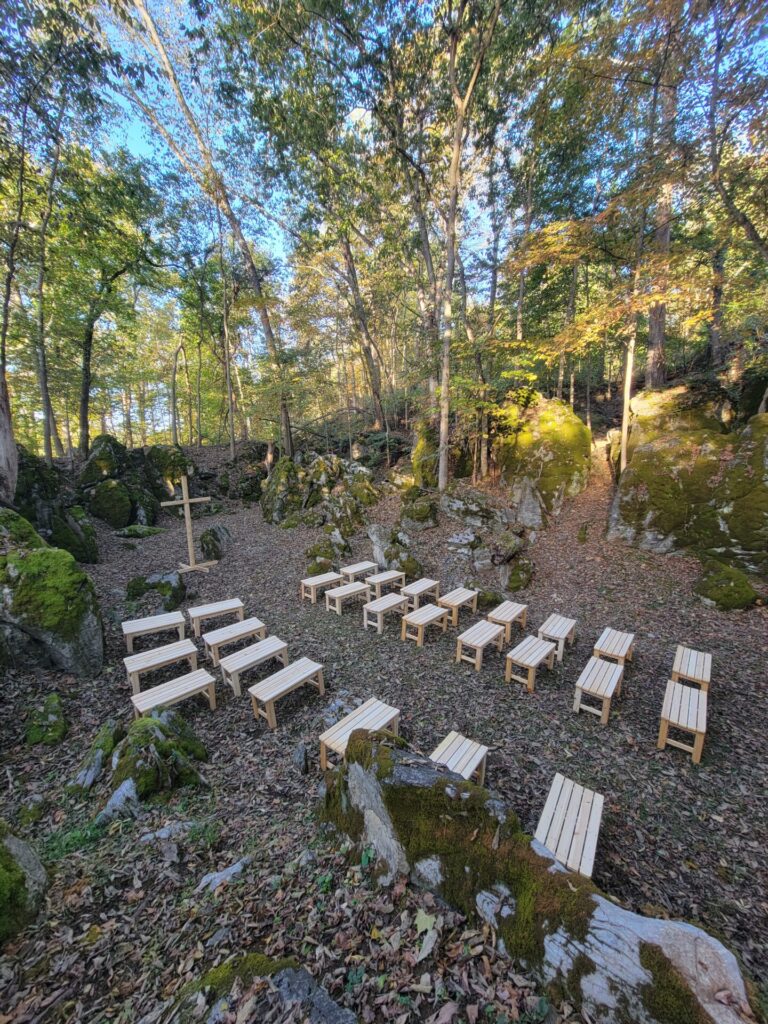 Woodland Outdoor Wedding Ceremony Location with handcrafted wooden benches surrounded by mature trees, moss-covered rocks, and natural stone formations at Timber Valley Farm Barn Rental in Clear Spring Maryland.