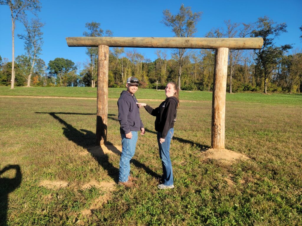Engaged couple standing beneath the handcrafted Wedding Ceremony Arbor at Timber Valley Farm Barn Rental in Clear Spring, Maryland. Outdoor Wedding Ceremony Ideas.