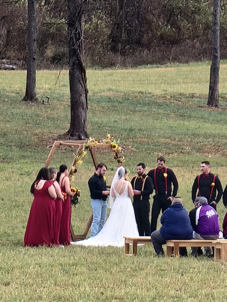 Outdoor Wedding Backdrop with ceremony structure, couple, wedding party, and open countryside at Timber Valley Farm Barn Rental in Clear Spring, Maryland.