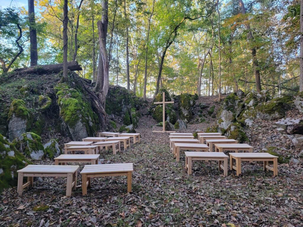 Wedding Ceremony Tips featuring the outdoor ceremony site in God's Cathedral at Timber Valley Farm Barn Rental with wooden benches and a wooden cross in Clear Spring, Maryland.