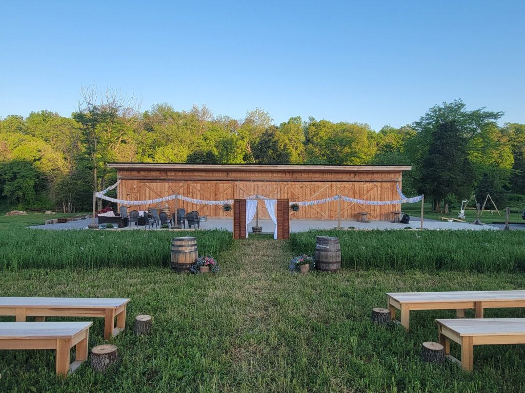 Outdoor Wedding Ceremony Location with wooden ceremony benches facing the timber-frame barn across the lawn at Timber Valley Farm Barn Rental in Clear Spring Maryland.