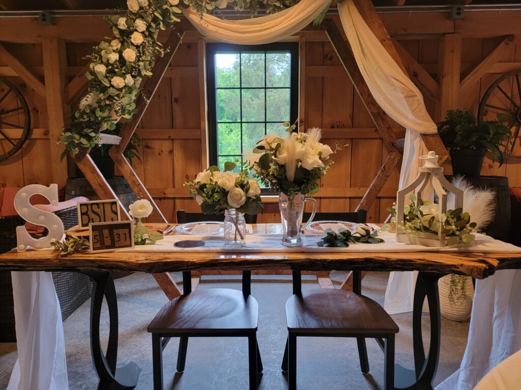 Wedding backdrop ideas featuring a decorated Hexagon Wedding Backdrop with a handcrafted Live Edge Sweetheart Table, personalized initials, white floral arrangements, and flowing fabric inside the timber-frame barn at Timber Valley Farm Barn Rental in Clear Spring, Maryland.