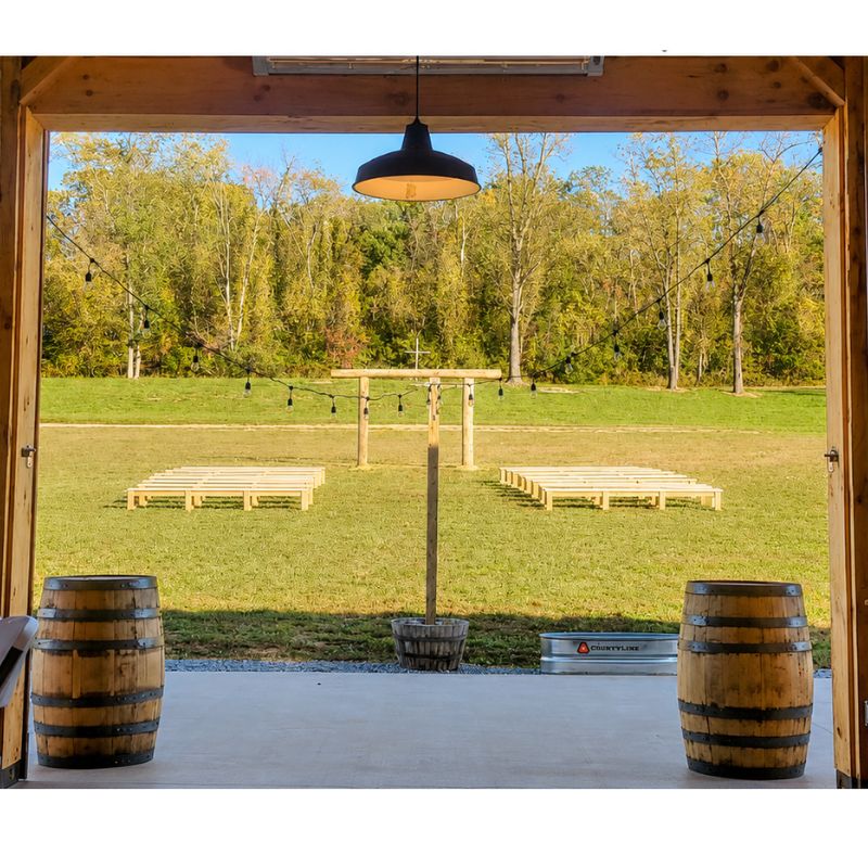 Outdoor Wedding Ceremony Locations featuring the Wedding Ceremony Arbor and wooden ceremony benches across the lawn, viewed from the timber-frame barn at Timber Valley Farm Barn Rental in Clear Spring Maryland.