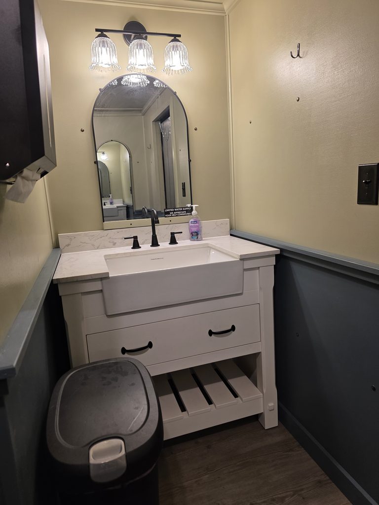 Elegant vanity area with modern sinks, mirrors, countertops, and decorative lighting inside the luxury restroom trailer available as an optional event upgrade at Timber Valley Farm Barn Rental in Clear Spring, Maryland.